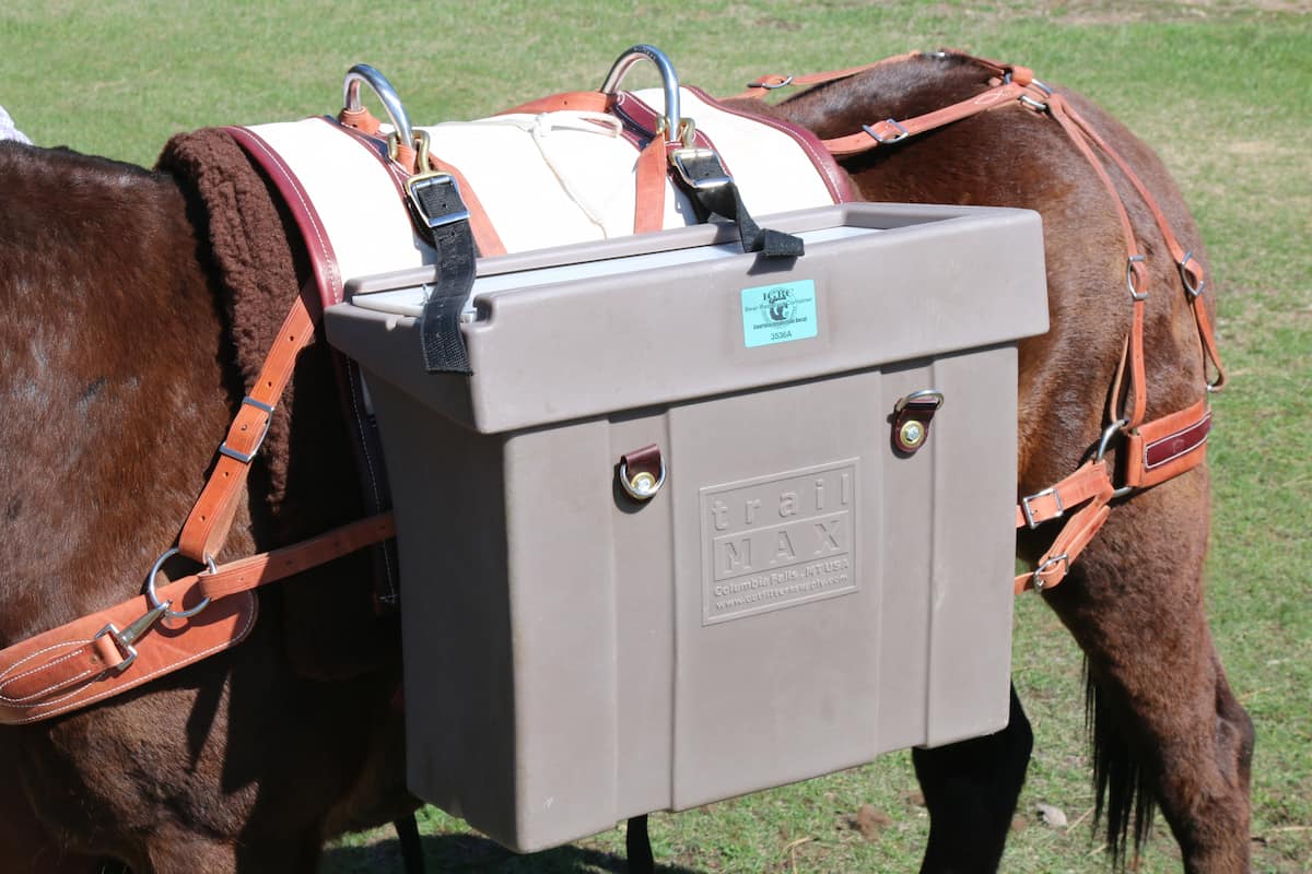 Hard-sided pannier attached to a Decker packs saddle with Decker hooks on a mule with grass in the background