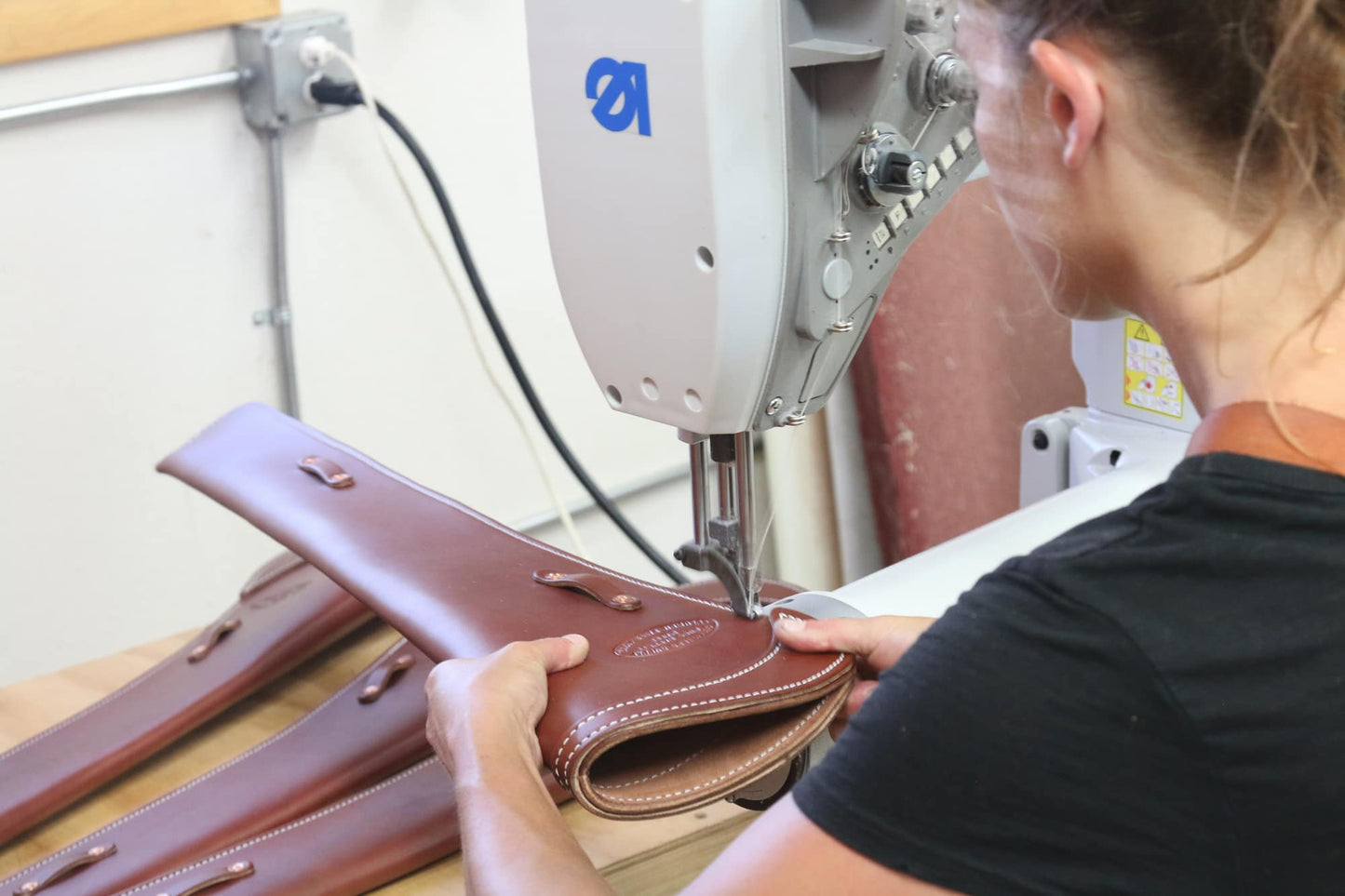Closeup of woman adding stitching to a leather carbine scabbard with a sewing machine