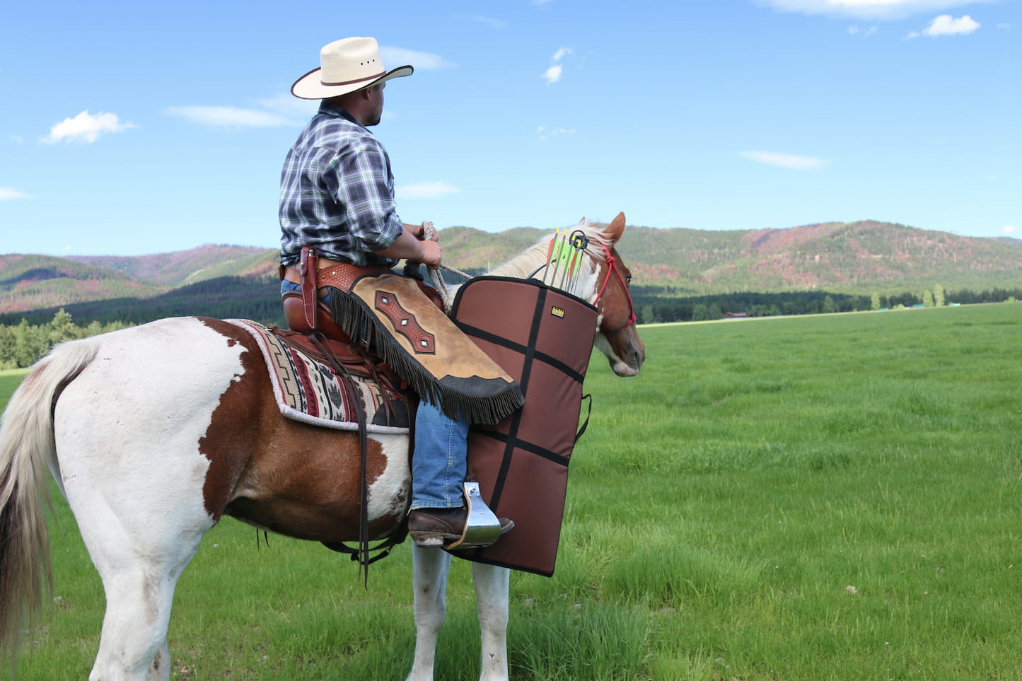 Man on brown and white horse wearing chinks with brown bow scabbard hanging off of riding saddle