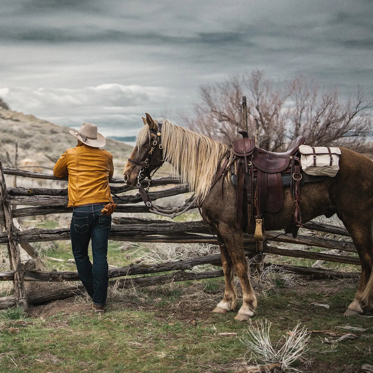 Man standing beside his horse with canvas saddlebags on a a saddle