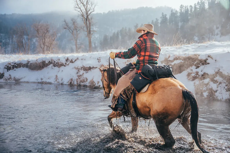 Man riding horse across a creek in the winter with saddlebags on the rear of his saddle