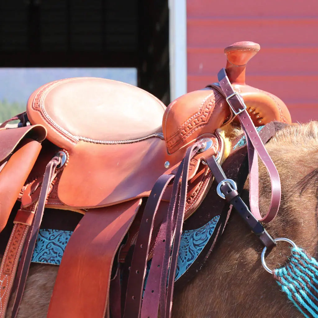 closeup of a McCall saddle on a horse in front of a red barn
