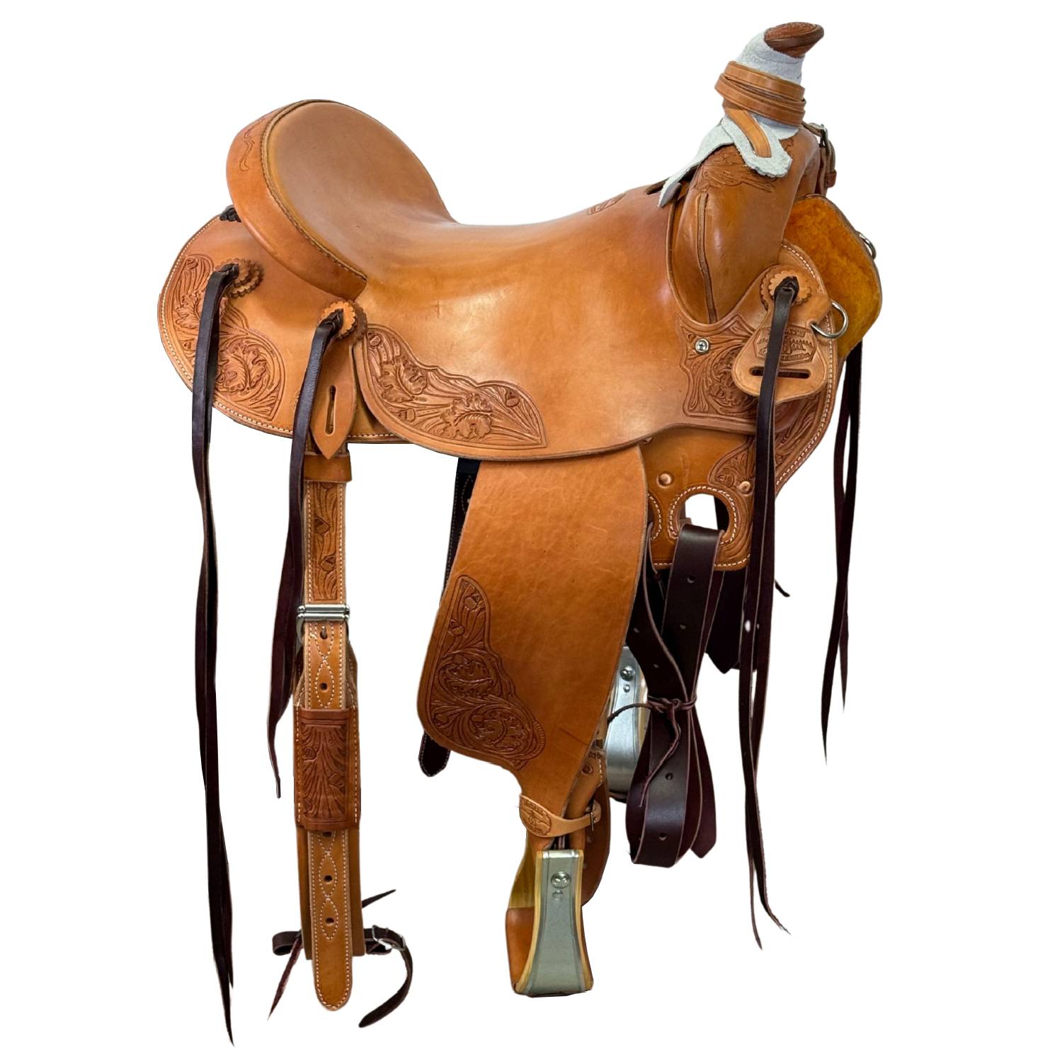 A classic brown leather western saddle with intricate hand-tooled floral patterns, black leather straps, and silver metal hardware, isolated on a white background.